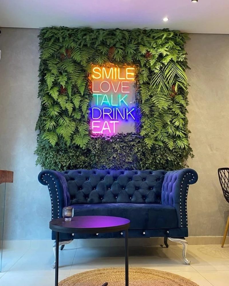 Lounge com painel de plantas artificiais e letreiro neon colorido