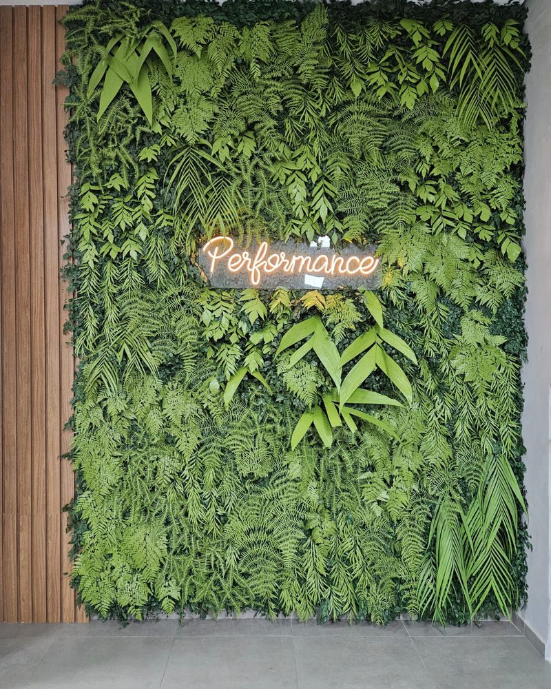 Parede de plantas artificiais de grande porte com letreiro neon na academia Performance
