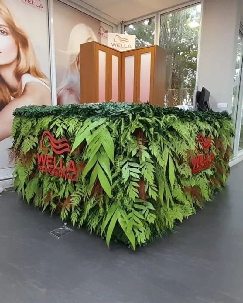 Balcão de evento revestido de folhagem artificial com logo Wella